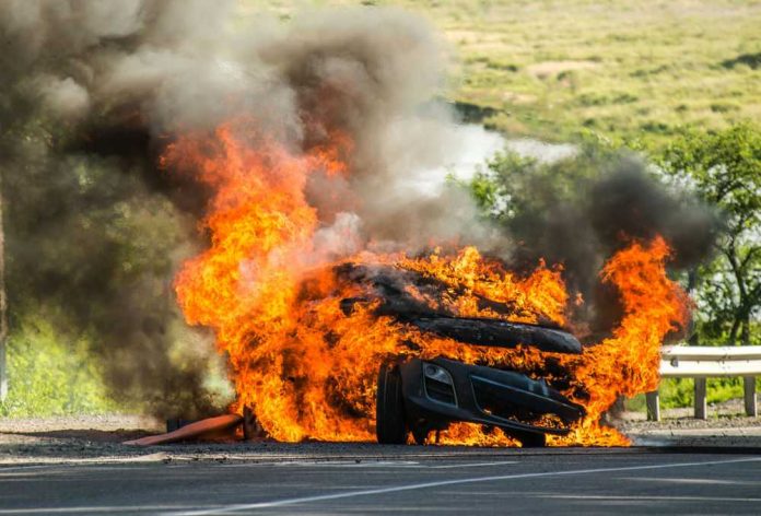 Burning car with flames and smoke on roadside