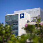 Doctors WARNING — We Cannot COMPLY Modern hospital building with a prominent H sign against a clear blue sky