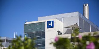 Doctors WARNING — We Cannot COMPLY Modern hospital building with a prominent H sign against a clear blue sky