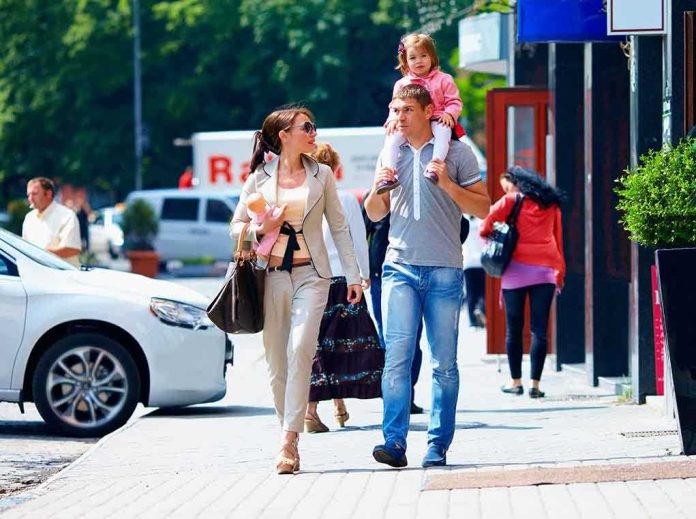 shutterstock_141816769 A family walking on a sidewalk in an urban area, with a child on the fathers shoulders