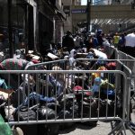 HOMELESS Bureau GUTTED — Where’d $300M Go? A crowded street with individuals sitting behind barriers and bags, highlighting urban homelessness