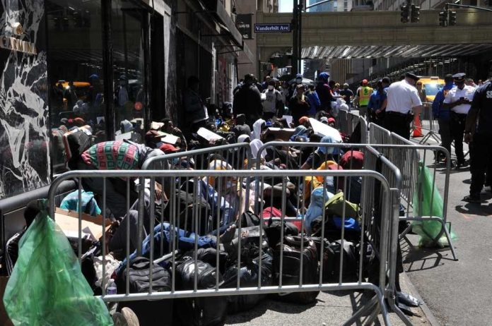 shutterstock_2341459009 A crowded street with individuals sitting behind barriers and bags, highlighting urban homelessness
