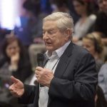 BOMBSHELL — Soros’ BLITZ Warps 2026 Map An elderly man speaking into a microphone at a conference with an attentive audience