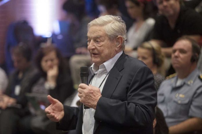 An elderly man speaking into a microphone at a conference with an attentive audience