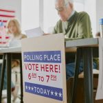 NONCITIZEN Voting BOMBSHELL Ignites The FEDS! Polling station with people voting, American flags visible.