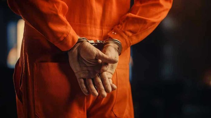 2056434935 Person in orange jumpsuit with handcuffs behind back.