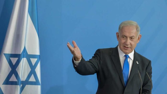 2276731307 Man in suit gestures beside Israeli flag.