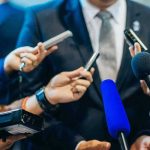REVEALED — Therapist’s Emails IGNITE Political Firestorm Journalists holding microphones interview a person in a suit.
