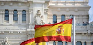 Trump TARGETS Spain — Huge Reason WHY! Two Spanish flags waving in front of a historic building