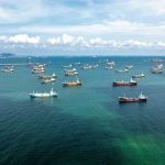 NEW IMMINENT THREATS — Oil Lifeline Held HOSTAGE Aerial view of numerous cargo ships anchored in a blue ocean