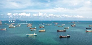 NEW IMMINENT THREATS — Oil Lifeline Held HOSTAGE Aerial view of numerous cargo ships anchored in a blue ocean