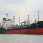 NEW Hormuz Inferno ROCKS The GLOBE! A cargo ship navigating through a port with industrial buildings in the background