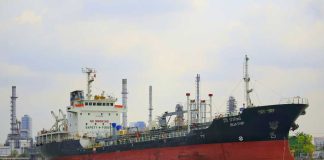 NEW Hormuz Inferno ROCKS The GLOBE! A cargo ship navigating through a port with industrial buildings in the background