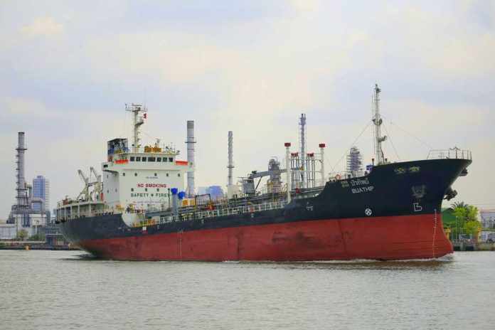 shutterstock_2644702975 A cargo ship navigating through a port with industrial buildings in the background