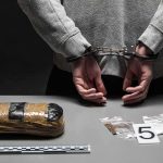 ISIS Pledge — NEW BOMB Plot Exposed person in handcuffs behind back over table with seized packages