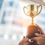 Award Winner Tied to TRAFFICKING RING! Hands holding a golden trophy cup