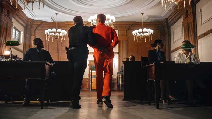 Prisoner in orange jumpsuit escorted by officer in a courtroom