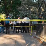 Park HORROR — Masked GUNMEN Ambush Crowd Police officers gather behind yellow tape on a tree-lined sidewalk