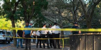 Park HORROR — Masked GUNMEN Ambush Crowd Police officers gather behind yellow tape on a tree-lined sidewalk