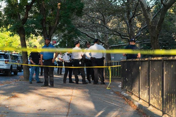 shutterstock_2058371216 Police officers gather behind yellow tape on a tree-lined sidewalk