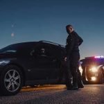 Why Cops Tap Your Trunk — CHILLING REASON Police officer stands beside a stopped car at dusk
