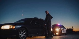 Why Cops Tap Your Trunk — CHILLING REASON Police officer stands beside a stopped car at dusk