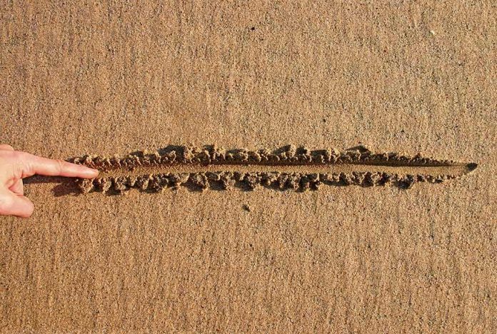 Finger drawing a straight line in wet sand