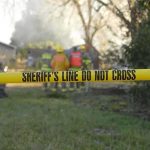 Wildfire Whodunit — BIZARRE Arrest DETAILS REVEALED Yellow police tape marking a restricted area at a fire scene with firefighters in the background