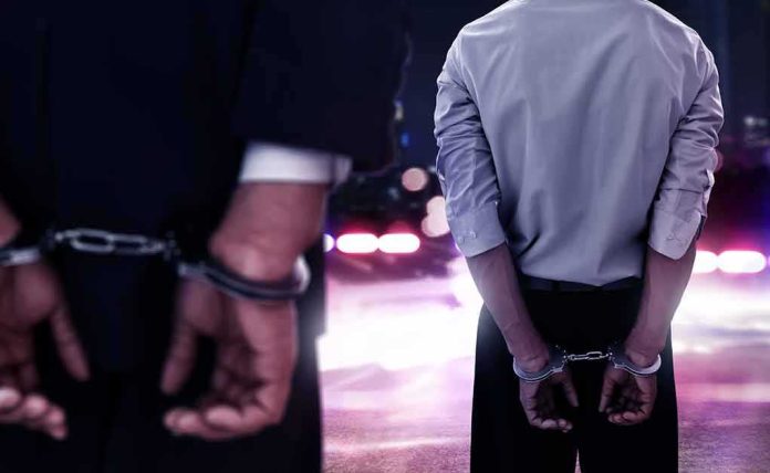 Two men in handcuffs with police lights in the background