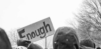 The UK Just Got A Breakup Letter — Signed Three Times crowd in winter coats at a protest holding a sign