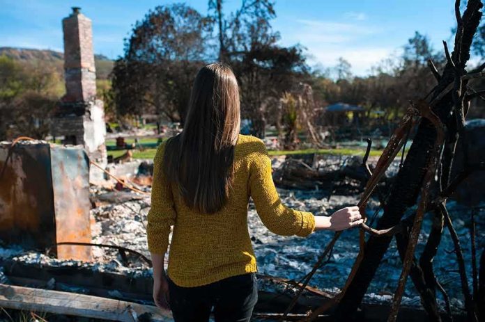 Woman in yellow sweater surveys burned ruins outdoors
