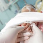 A Father Lay Beside His Dying Baby — And Said Three WORDS Gloved hands holding a baby's hand in a hospital bed