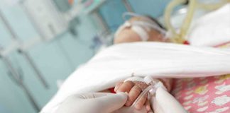A Father Lay Beside His Dying Baby — And Said Three WORDS Gloved hands holding a baby's hand in a hospital bed