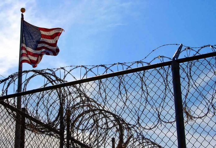 shutterstock_1218662-1 American flag near barbed wire fence against blue sky