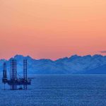 Trump CLAIMS 65B-Barrel Coup An oil rig in the ocean with a backdrop of mountains during sunset