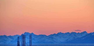 Trump CLAIMS 65B-Barrel Coup An oil rig in the ocean with a backdrop of mountains during sunset