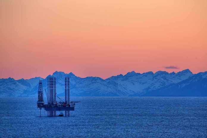 shutterstock_139270961 An oil rig in the ocean with a backdrop of mountains during sunset