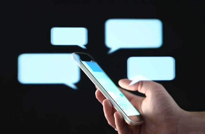shutterstock_1452139727-1 Hand holding smartphone with chat bubbles on dark background