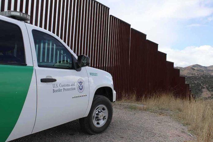 shutterstock_1478048393 Border patrol SUV parked beside tall steel border fence