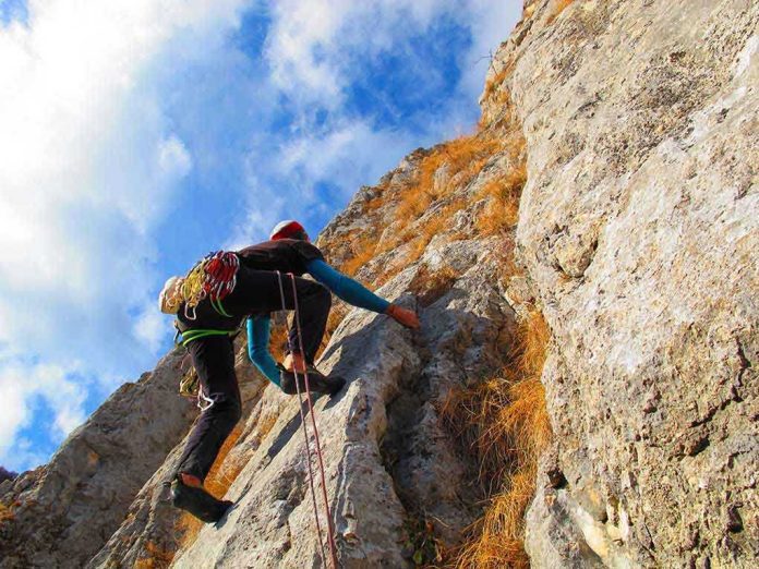 shutterstock_150995747 A climber ascending a rocky cliff under a blue sky