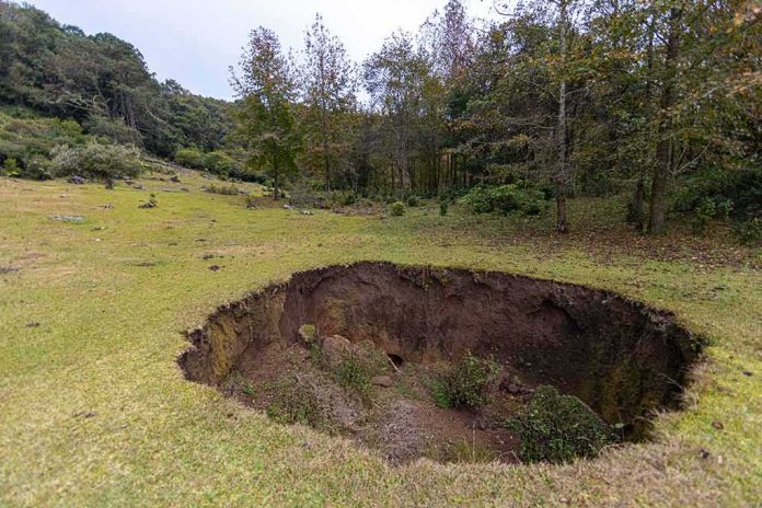 shutterstock_1684130278 Large sinkhole in a grassy field near a forest