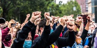 Protesters Stormed The Runway — Look Who Grabbed THEM Crowd of protesters with raised fists wearing masks