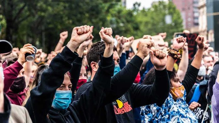 shutterstock_1902465079 Crowd of protesters with raised fists wearing masks
