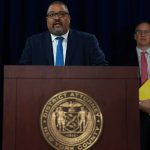 Weinstein Mistrial Again: Justice System in Crisis? Man speaks at podium with New York County District Attorney seal