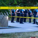 She Had A Restraining Order — He Had An AirTag. police officers stand behind caution tape at a park scene