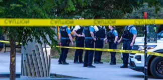 She Had A Restraining Order — He Had An AirTag. police officers stand behind caution tape at a park scene