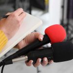 God Comment Haunts Talarico Journalist holding two microphones while writing in a notebook