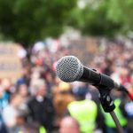 Candidate ATTACKED — Multiple INJURED microphone on stand in front of a blurred crowd