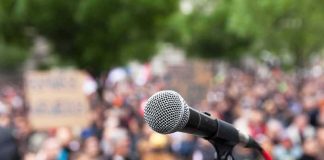 Candidate ATTACKED — Multiple INJURED microphone on stand in front of a blurred crowd