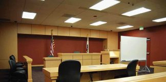 He Shot Three Students On A Sidewalk — Then He Opened His DOOR Interior view of an empty courtroom with wooden furniture and American flags